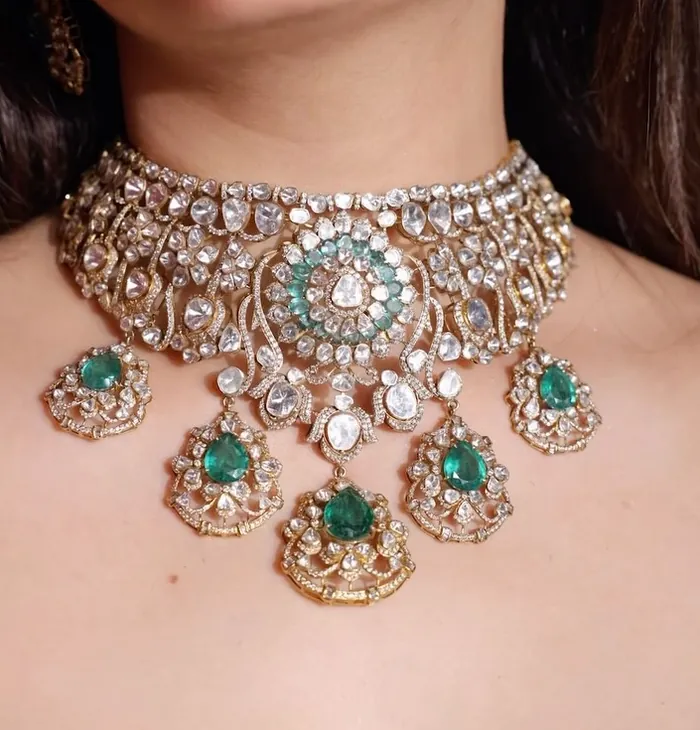 A wide gold choker set with pale and green stones, worn at the neck