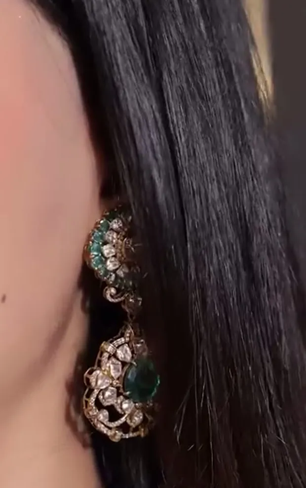 A long two-part gold earring set with green stones, worn against dark hair