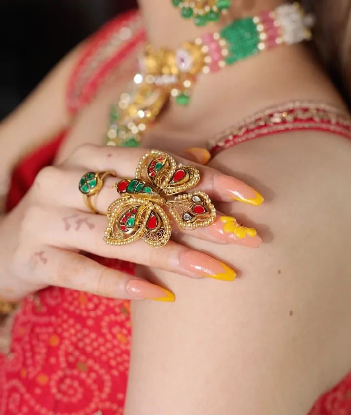 The Paarwaaz gold ring worn on a hand, with red and green stones set in gold